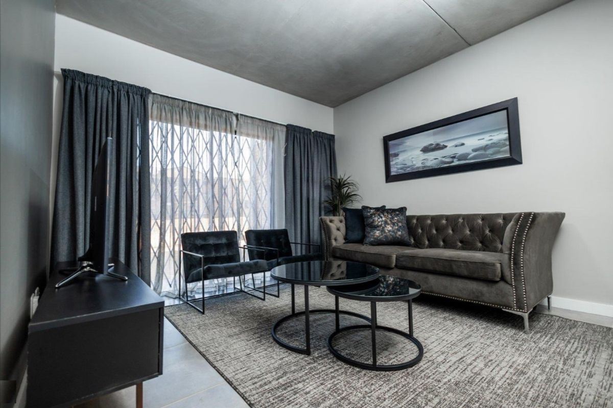 Modern living room featuring an exposed concrete ceiling, neutral walls, and a large sliding glass door with an integrated security gate.