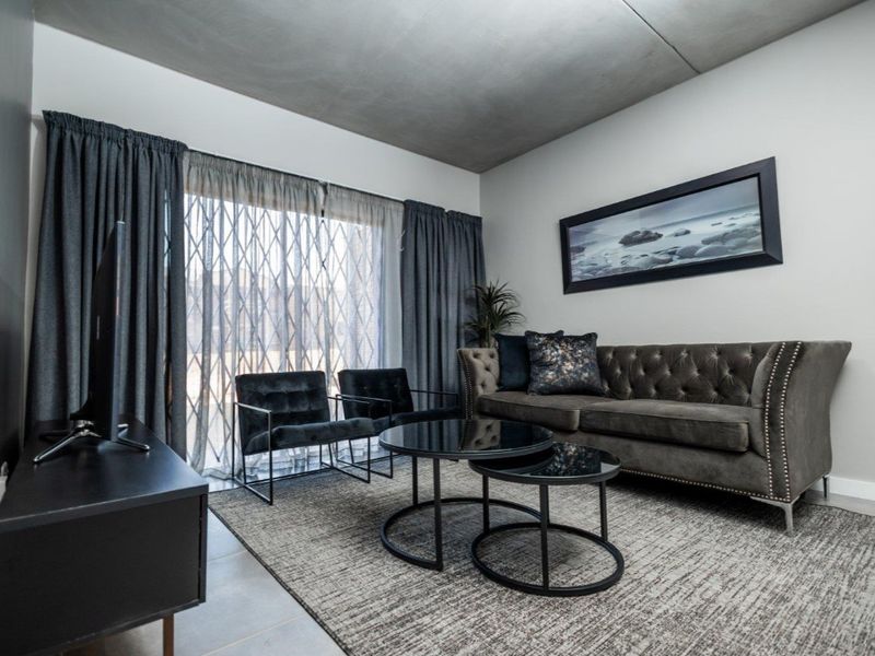 Modern living room featuring an exposed concrete ceiling, neutral walls, and a large sliding glass door with an integrated security gate.
