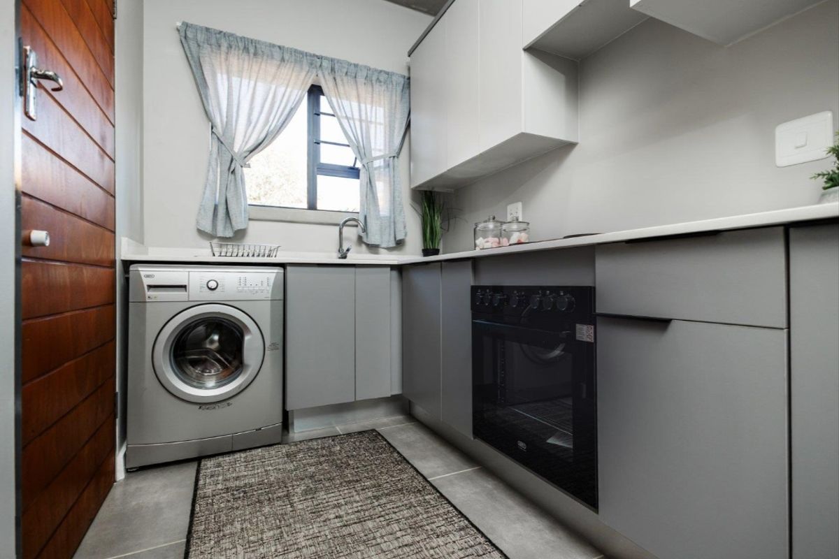 Modern kitchen featuring sleek grey cabinetry, stone countertops, built-in oven, hob, and integrated laundry plumbing in a compact, functional layout.