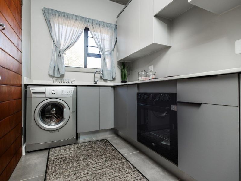 Modern kitchen featuring sleek grey cabinetry, stone countertops, built-in oven, hob, and integrated laundry plumbing in a compact, functional layout.