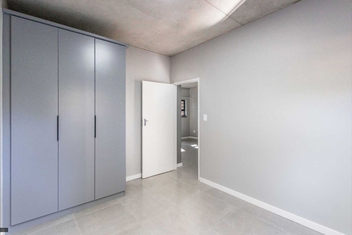 Modern bedroom featuring a sleek built-in wardrobe, neutral tiled flooring, and an exposed concrete ceiling, offering a clean and contemporary living space.