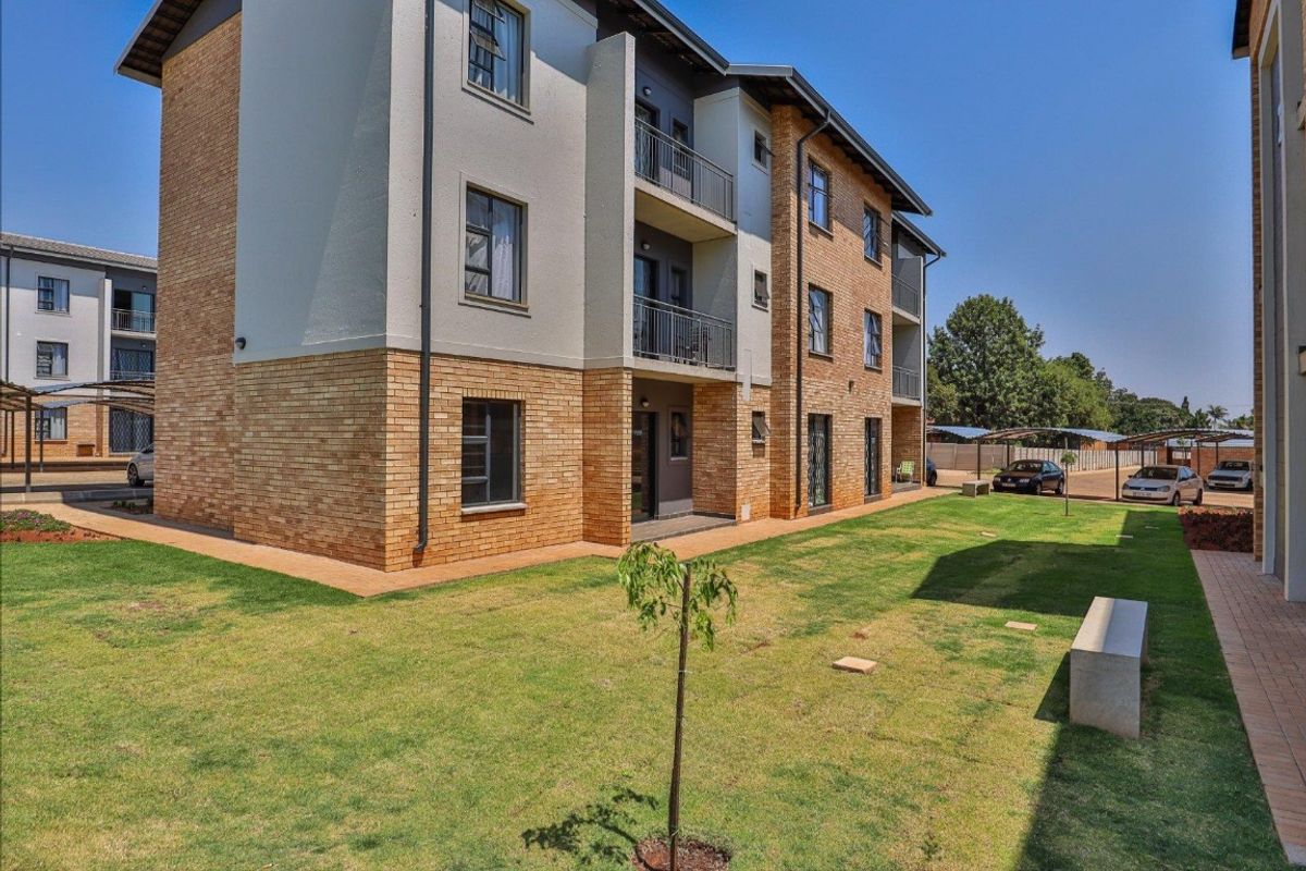 Exterior view of a modern apartment complex featuring face brick and plastered finishes, private balconies, and well-maintained communal garden areas with paved walkways.