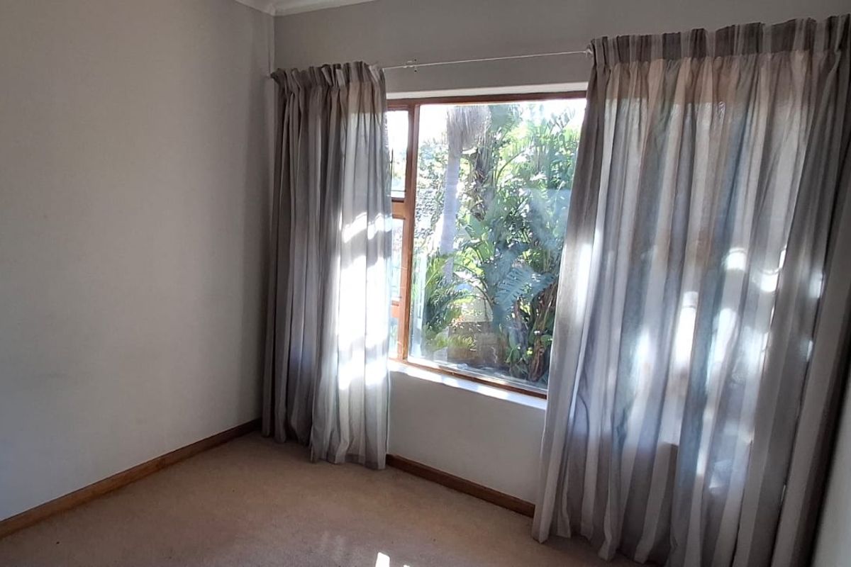 A bright, empty bedroom featuring carpeted flooring and a large window with curtains, offering a view of the garden.