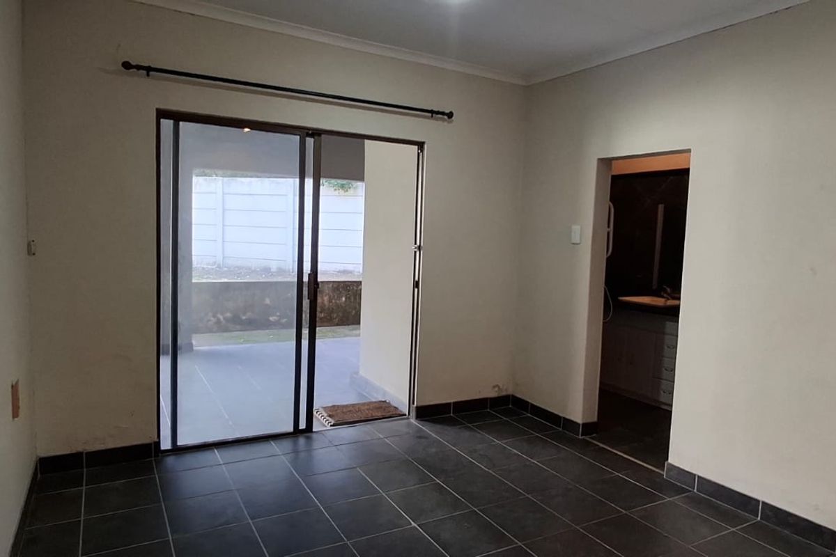 An empty bedroom featuring dark tiled flooring, a sliding glass door leading to an outdoor area, and direct access to an en-suite bathroom.