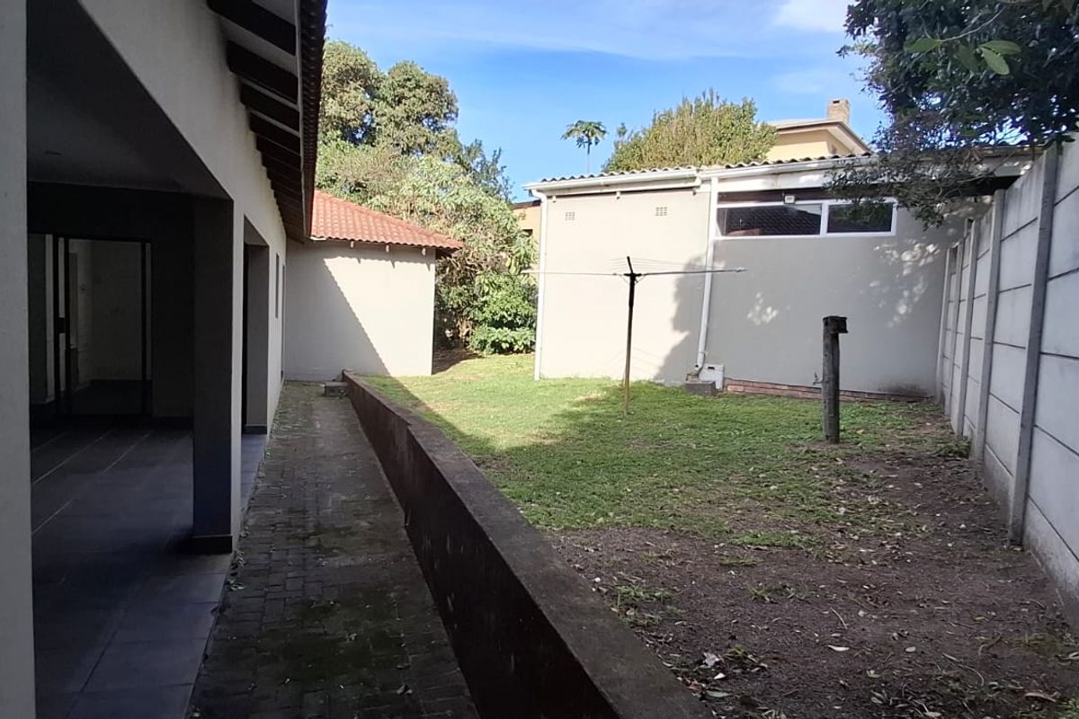 A rear exterior view featuring a paved walkway, a covered patio area, and a private garden enclosed by precast concrete boundary walls.