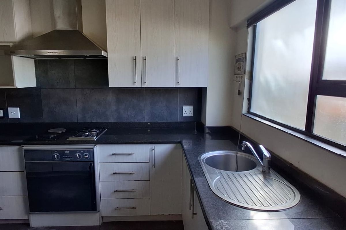 A functional kitchen featuring built-in cabinetry, granite countertops, a stainless steel sink, and integrated cooking appliances including an oven and gas hob.