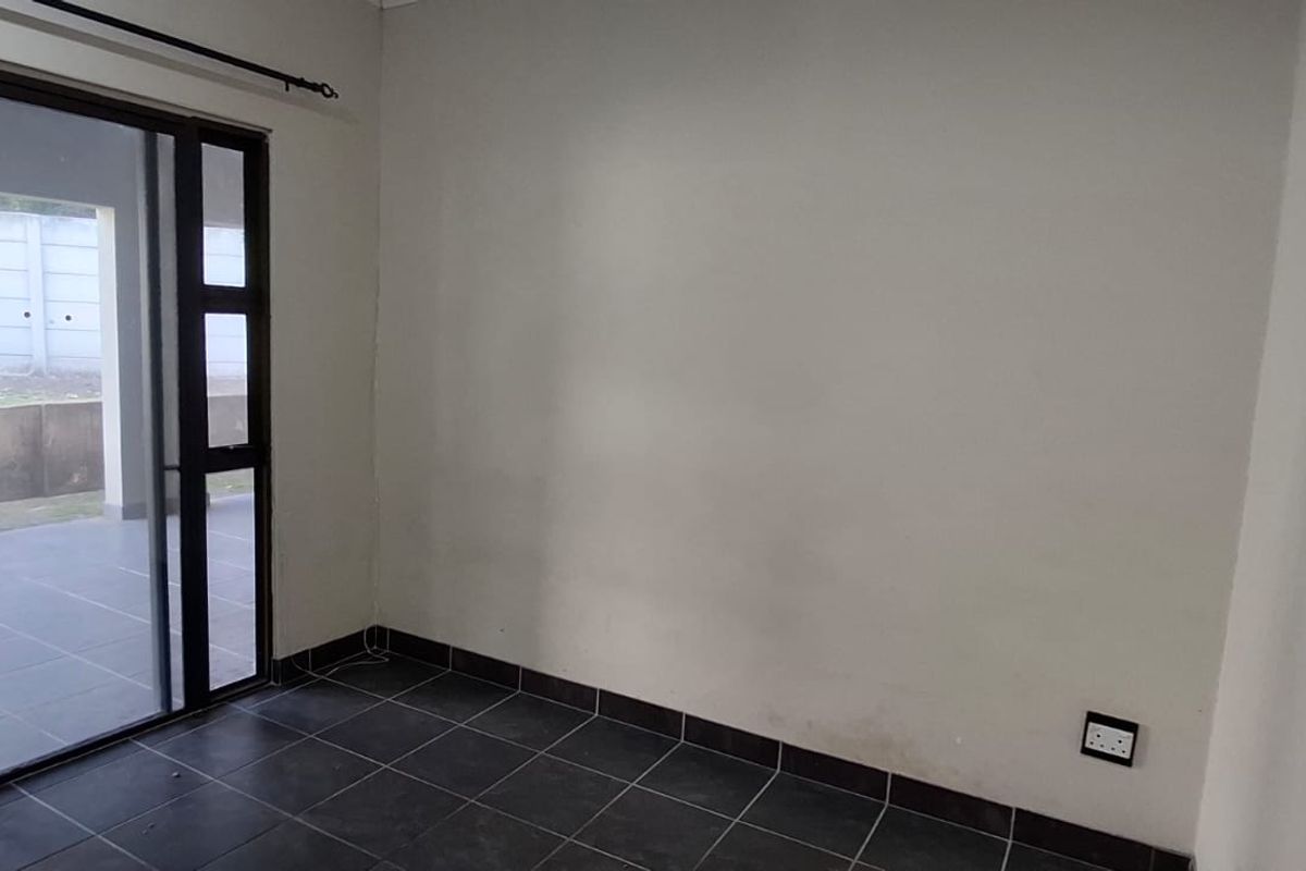 An empty living room featuring dark floor tiles and a large sliding glass door providing access to the outdoor patio area.