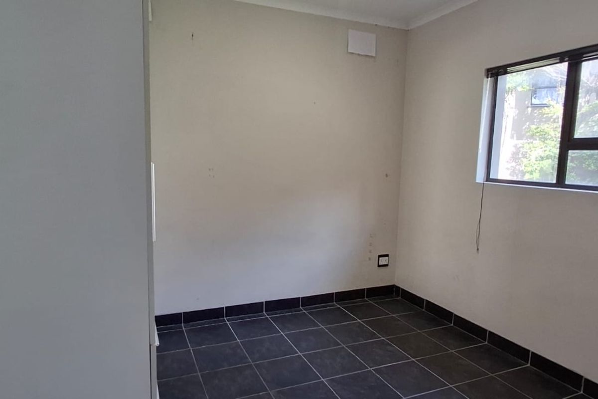 A vacant bedroom featuring dark tiled flooring, neutral walls, and a built-in cupboard, offering a blank canvas for personalization.