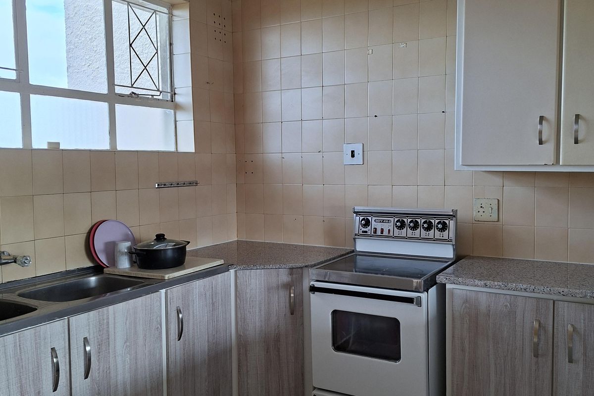 A functional kitchen featuring laminate cabinetry, granite-look countertops, a freestanding electric stove, and ceramic tile finishes throughout.