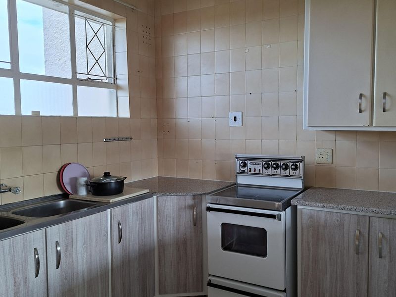 A functional kitchen featuring laminate cabinetry, granite-look countertops, a freestanding electric stove, and ceramic tile finishes throughout.