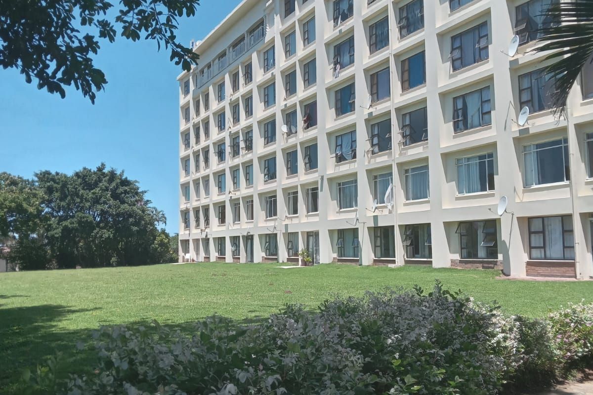 Exterior view of a multi-story apartment building featuring a large, well-maintained lawn and landscaped garden area.