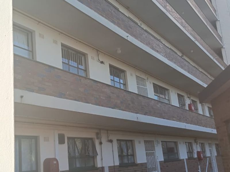 Exterior view of a multi-story apartment building featuring brick facade, open balconies, and a paved ground-level walkway.