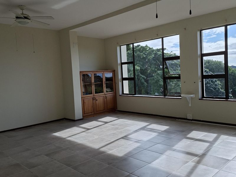 Spacious, light-filled living area featuring neutral tiled flooring, dual ceiling fans, and large windows offering pleasant views.