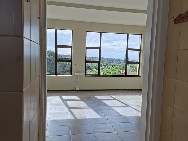 A bright, empty living area featuring large windows with scenic views and neutral tiled flooring, offering a blank canvas for interior design.