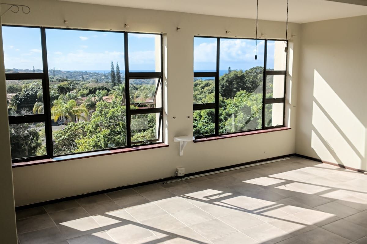 Bright and spacious living area featuring large windows with scenic views, neutral tiled flooring, and a ceiling fan.