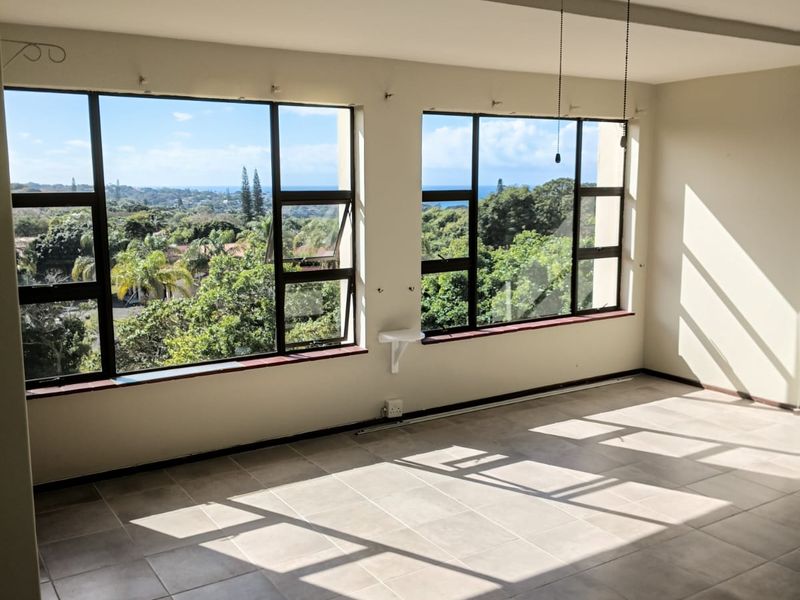 Bright and spacious living area featuring large windows with scenic views, neutral tiled flooring, and a ceiling fan.