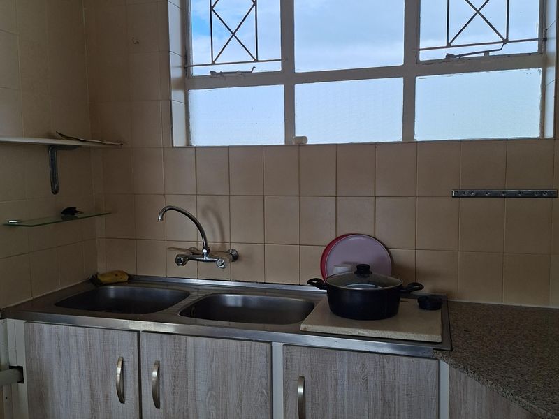 A functional kitchen area featuring a double bowl stainless steel sink, tiled splashbacks, and laminate cabinetry with a window providing natural light.
