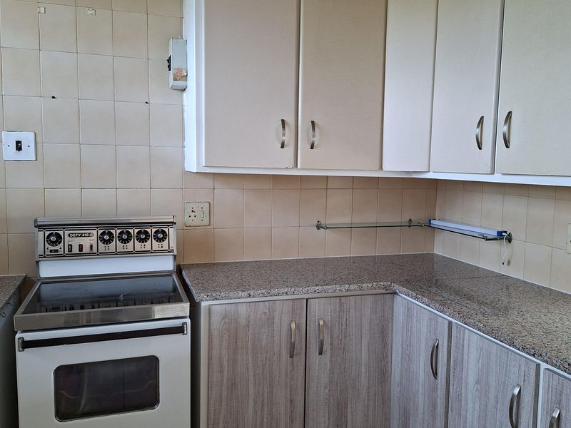 A dated kitchen featuring built-in cabinetry, laminate countertops, and a freestanding stove, with ceramic wall and floor tiling throughout.
