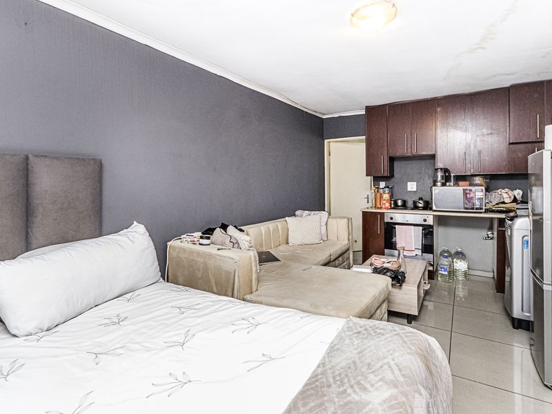 Compact open-plan studio apartment featuring a kitchenette with built-in cabinetry and oven, tiled flooring, and a combined living and sleeping area.