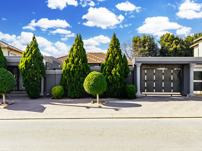 Front elevation of the property featuring a secure boundary wall, sliding gate, and paved driveway entrance.