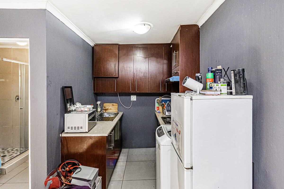 Compact kitchen featuring dark wood cabinetry, laminate countertops, and tiled flooring, with an adjacent view into a tiled bathroom area.