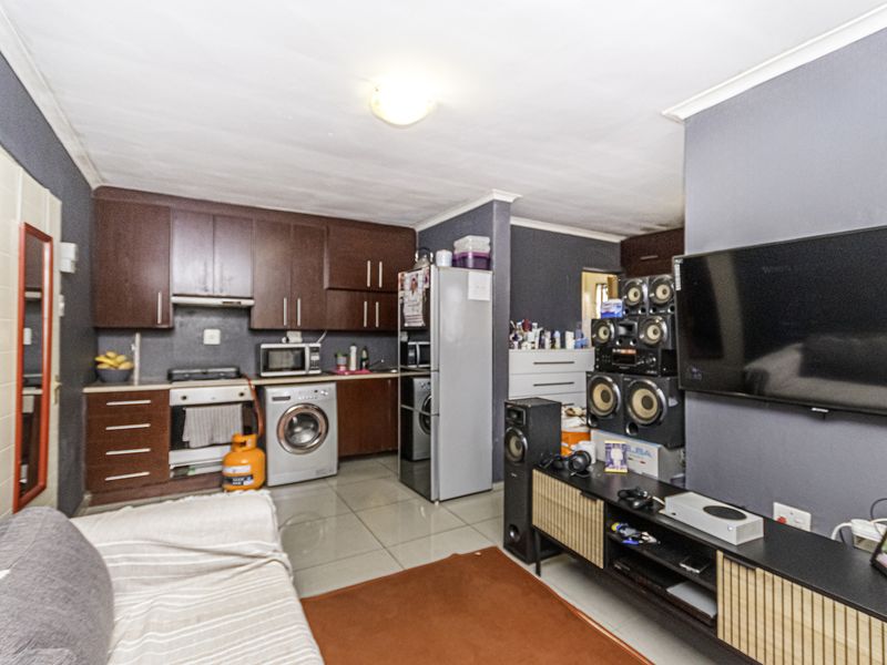 Open plan living area featuring a compact kitchen with dark wood cabinetry, gas stove, and tiled flooring, seamlessly integrated with the lounge space.