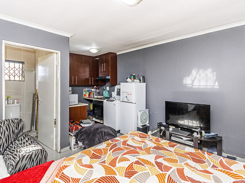 Open-plan living area featuring a compact kitchenette with built-in cabinetry, oven, and hob, adjacent to a bedroom space with access to an en-suite bathroom.