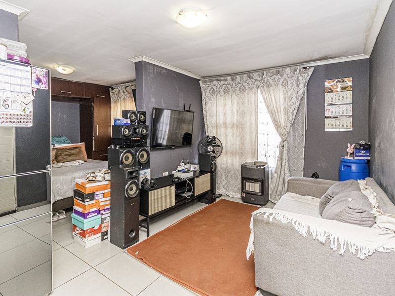 Open plan living and bedroom area featuring tiled flooring and built-in storage, showing signs of wear and ceiling water damage.