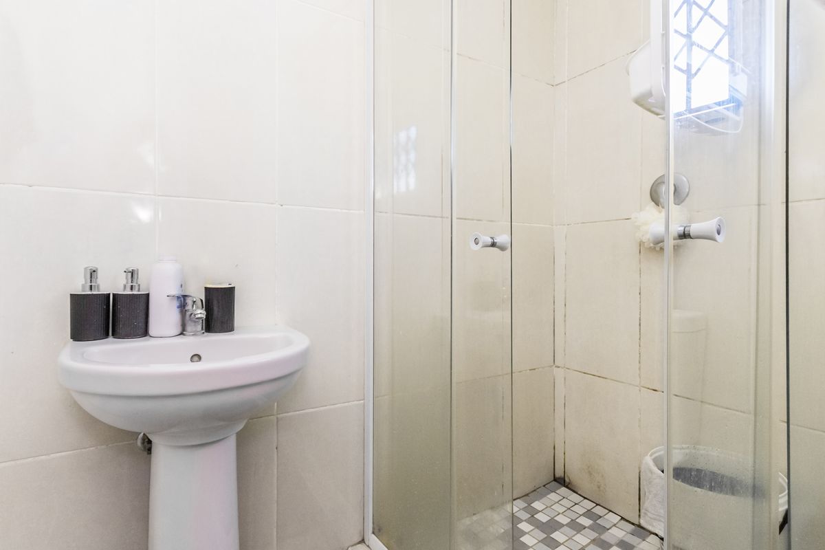 A compact bathroom featuring a pedestal basin and a glass-enclosed shower with tiled finishes.