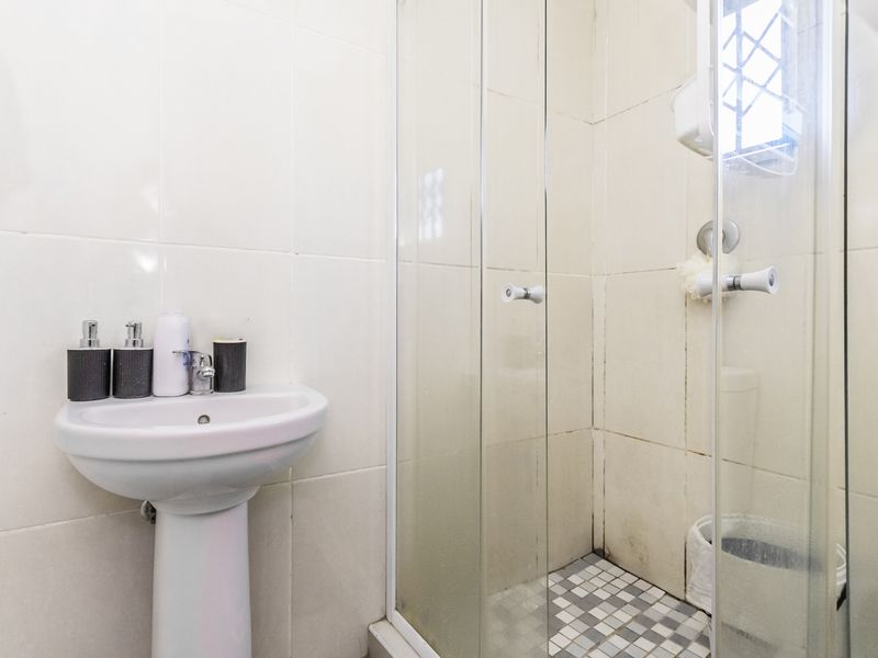 A compact bathroom featuring a pedestal basin and a glass-enclosed shower with tiled finishes.