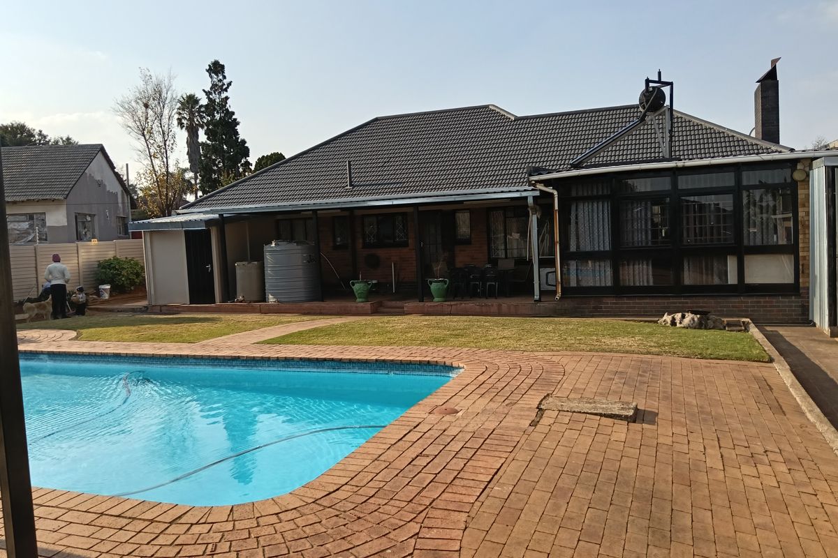 Rear view of the property featuring a swimming pool, brick-paved patio area, and an enclosed sunroom extension with a tiled roof.