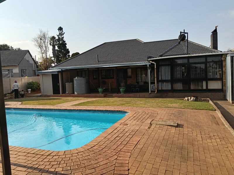 Rear view of the property featuring a swimming pool, brick-paved patio area, and an enclosed sunroom extension with a tiled roof.