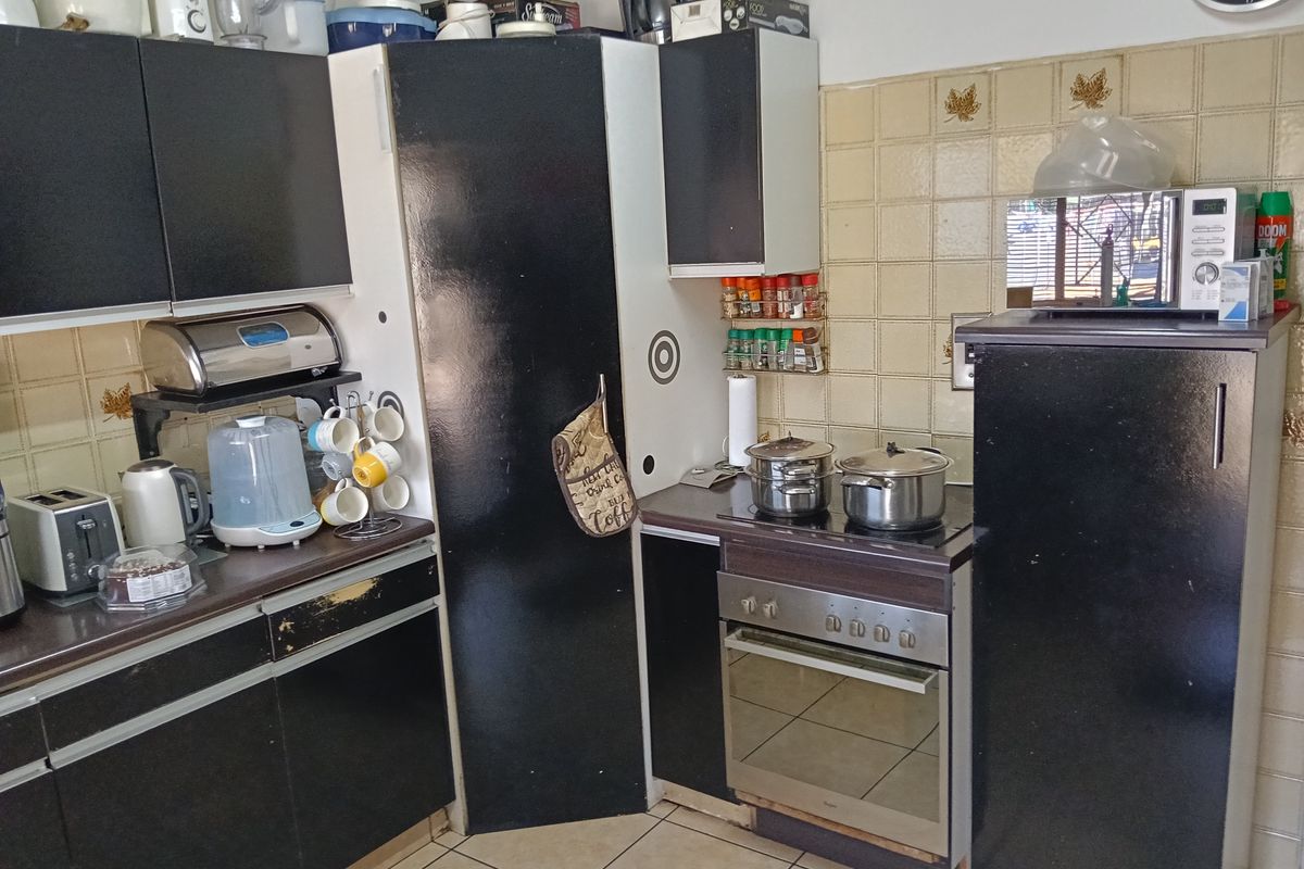 A compact kitchen featuring black cabinetry, tiled backsplash, and built-in oven with electric hob, showing signs of wear and dated finishes.