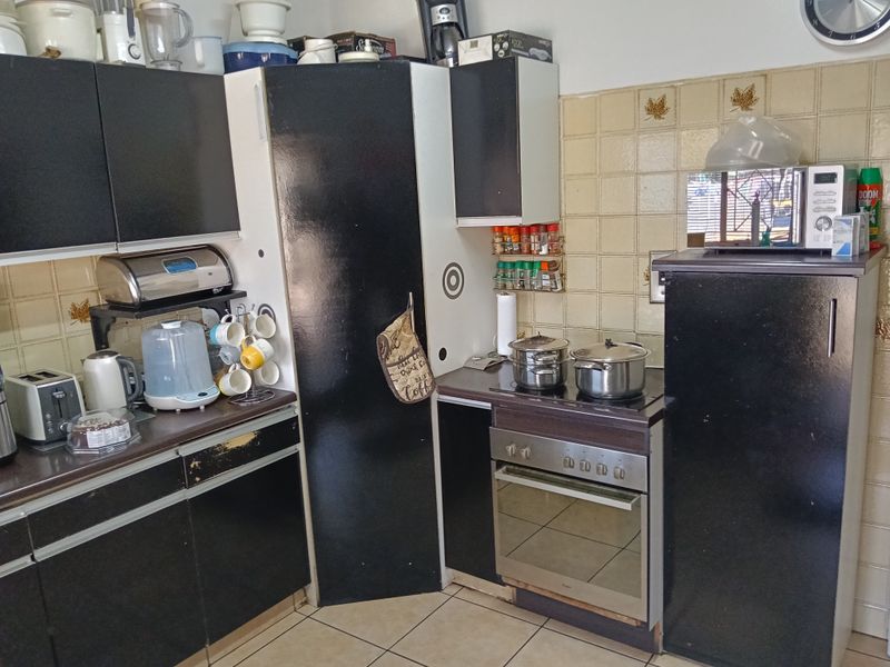 A compact kitchen featuring black cabinetry, tiled backsplash, and built-in oven with electric hob, showing signs of wear and dated finishes.