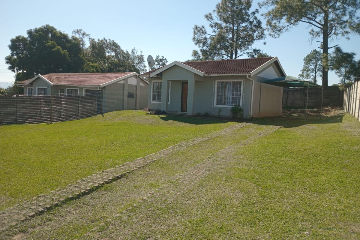 Front view of a detached townhouse featuring a tiled roof, paved driveway, and surrounding lawn area.