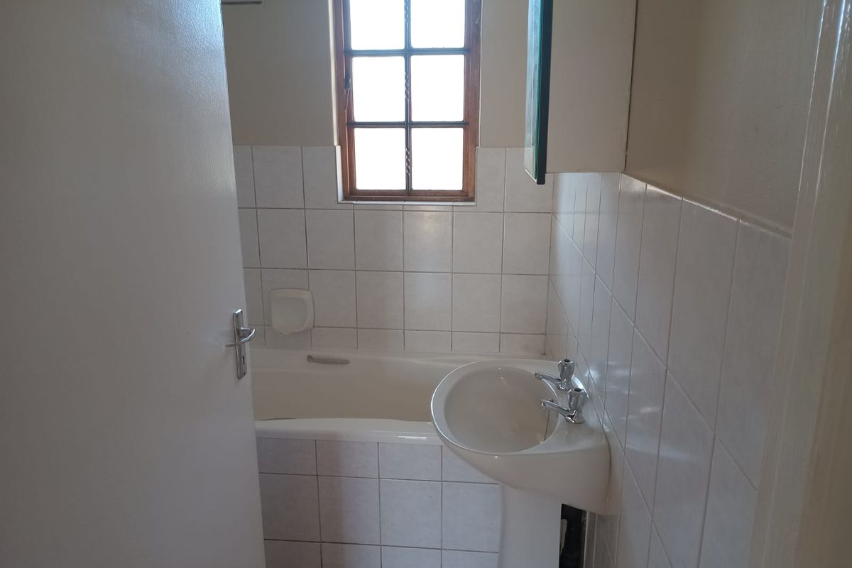 A functional bathroom featuring a pedestal basin, built-in bathtub, and tiled walls, offering a clean and simple layout ready for modernization.