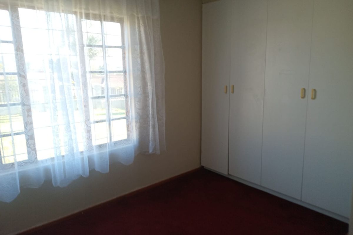 A vacant bedroom featuring built-in cupboards, carpeted flooring, and a window with security bars.