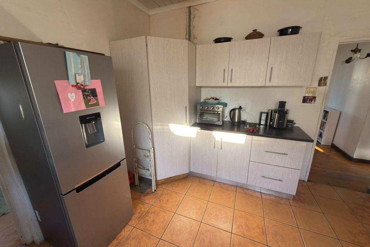 A compact kitchen featuring light-toned laminate cabinetry, dark countertops, and ceramic floor tiles, requiring some cosmetic wall repairs.