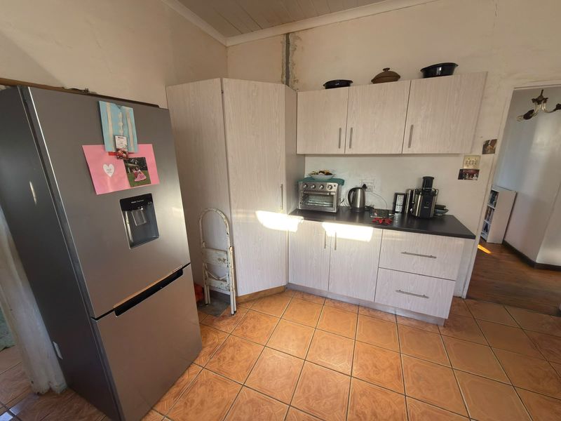 A compact kitchen featuring light-toned laminate cabinetry, dark countertops, and ceramic floor tiles, requiring some cosmetic wall repairs.