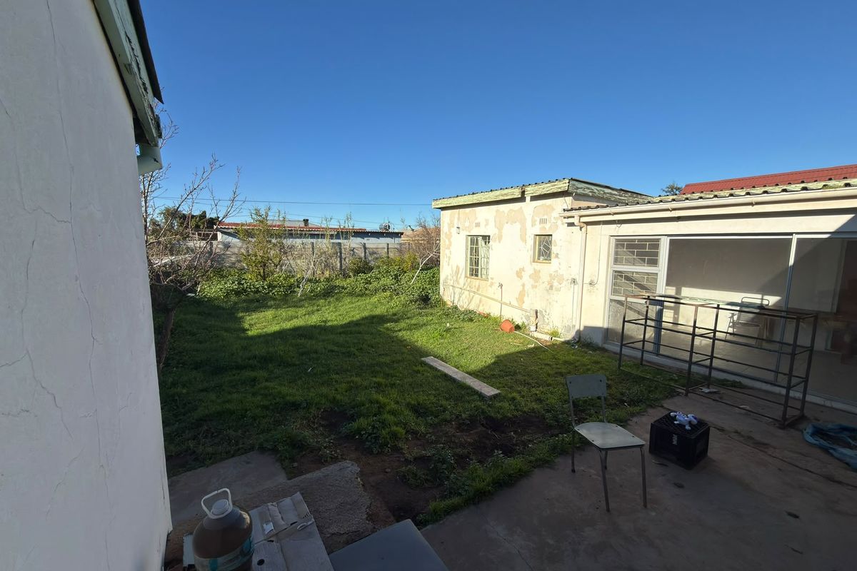 Rear exterior view of the property featuring a concrete patio, lawn area, and a building with visible exterior wall maintenance requirements.
