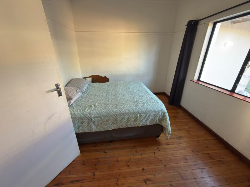 A bedroom featuring original timber flooring and a window with security bars, requiring minor cosmetic updates to walls and doors.