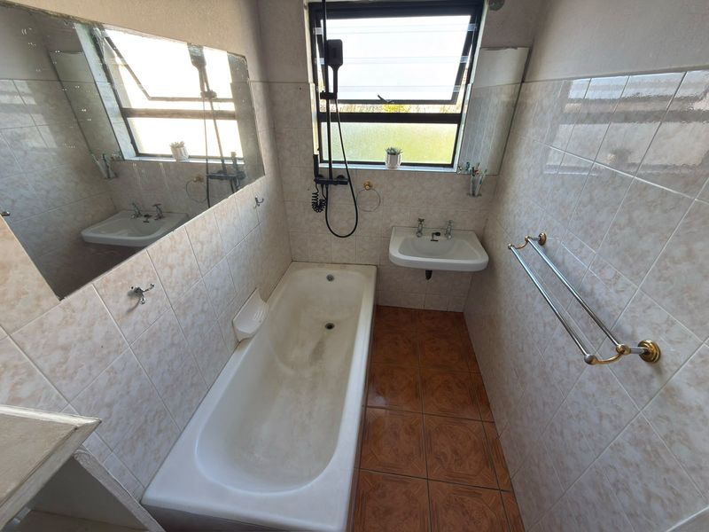 A compact bathroom featuring a bathtub, wall-mounted basin, and tiled finishes. The space is functional but would benefit from modern updates.
