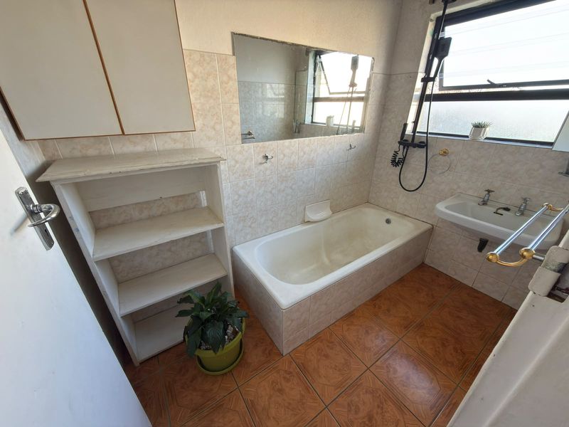 A dated bathroom featuring a built-in bathtub, wall-mounted basin, and tiled finishes. The space offers a functional layout ready for modern renovation.