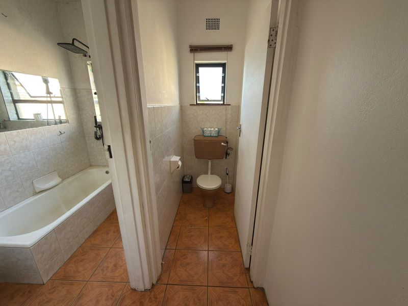 A dated bathroom featuring a bathtub with shower head and a separate toilet area with tiled finishes throughout.