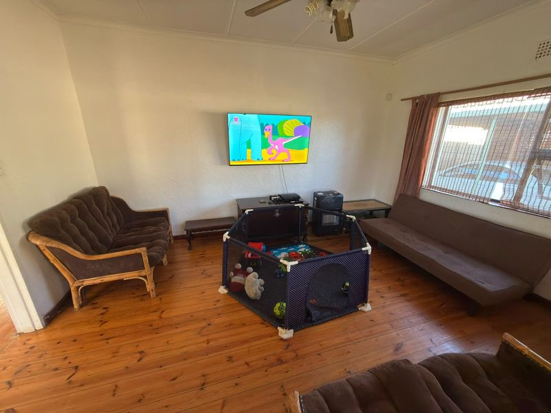A living room featuring polished timber flooring, a ceiling fan, and a large window providing natural light.