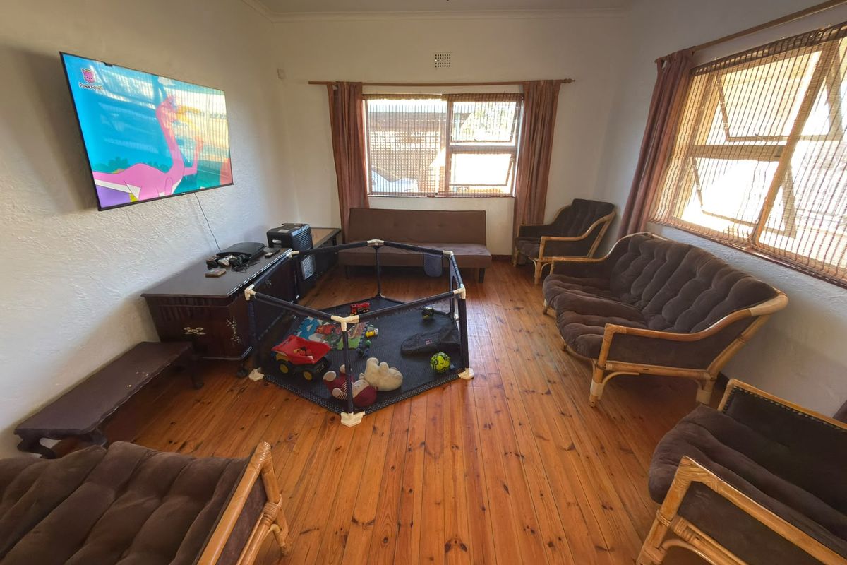 A spacious living room featuring warm timber flooring, a ceiling fan, and large windows that provide ample natural light.