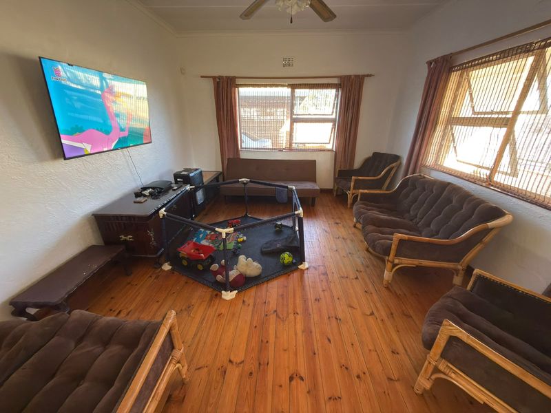 A spacious living room featuring warm timber flooring, a ceiling fan, and large windows that provide ample natural light.