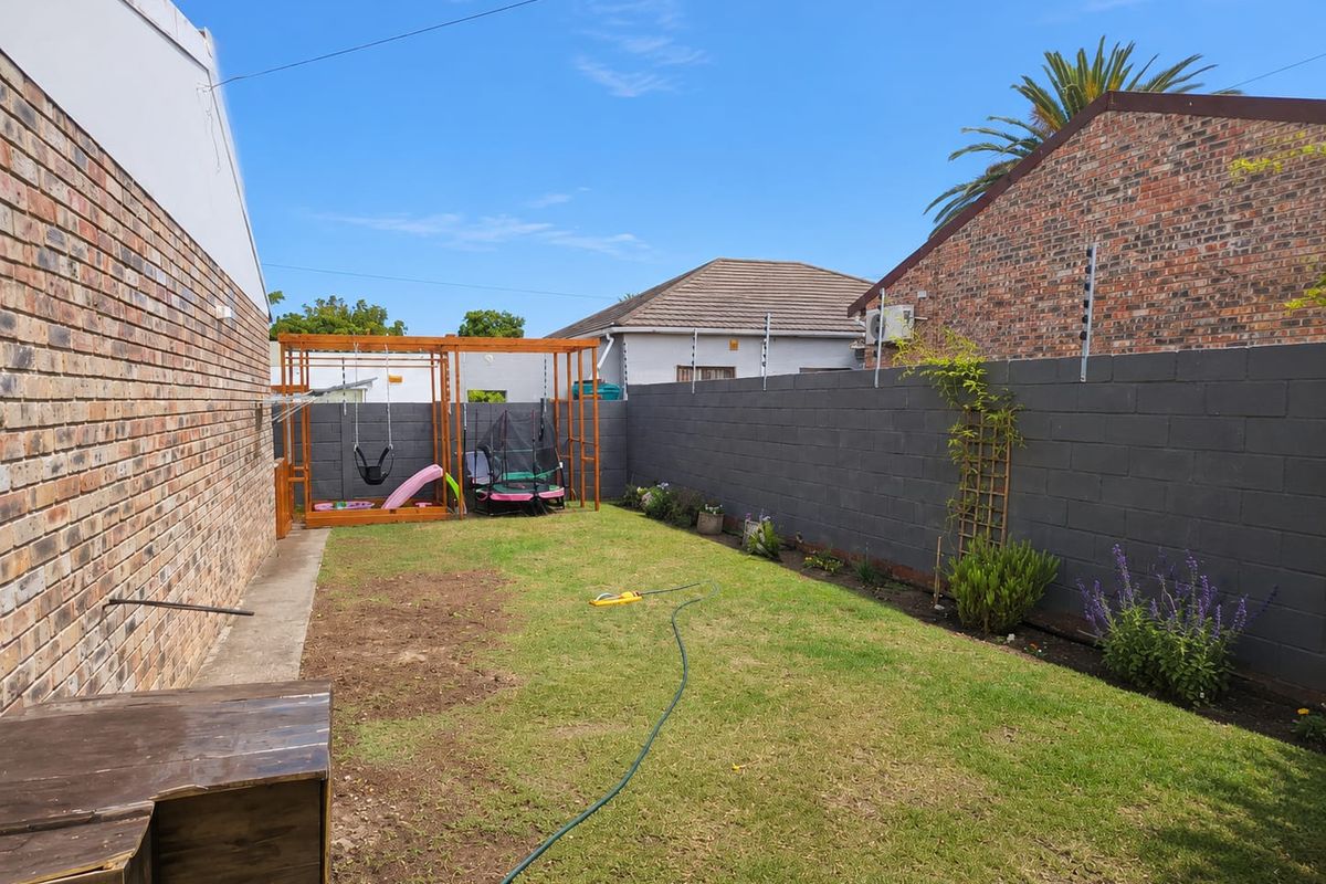 A private rear garden featuring a lawn area, enclosed by a brick boundary wall with integrated electric fencing.