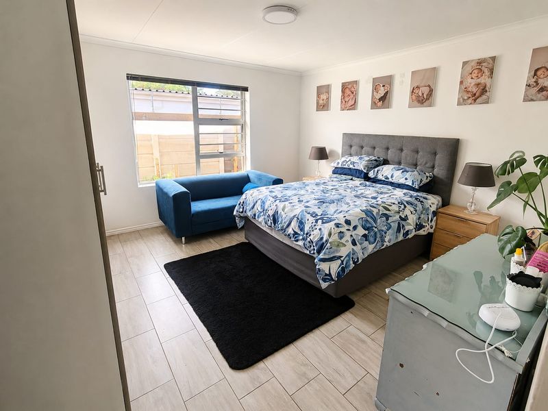A well-maintained bedroom featuring light-toned tiled flooring, neutral walls, and a large window providing natural light.