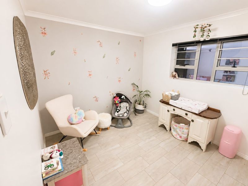 A well-maintained bedroom featuring neutral tiled flooring, clean wall finishes, and aluminium window frames, currently utilized as a nursery.